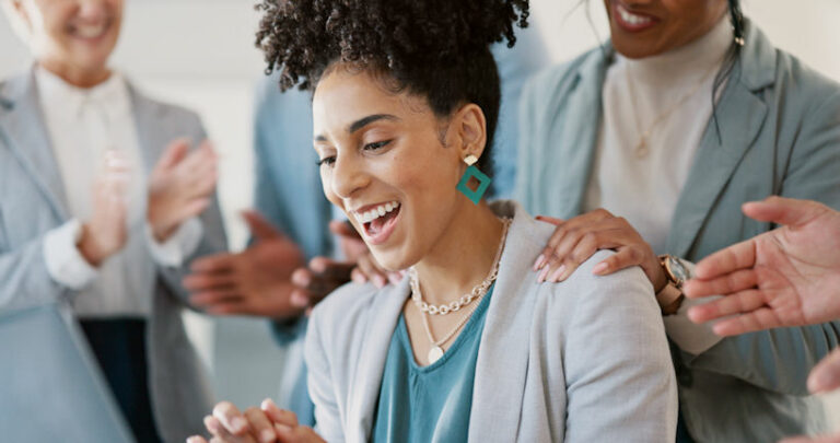 A woman smiling being congratulated by her coworkers around her.