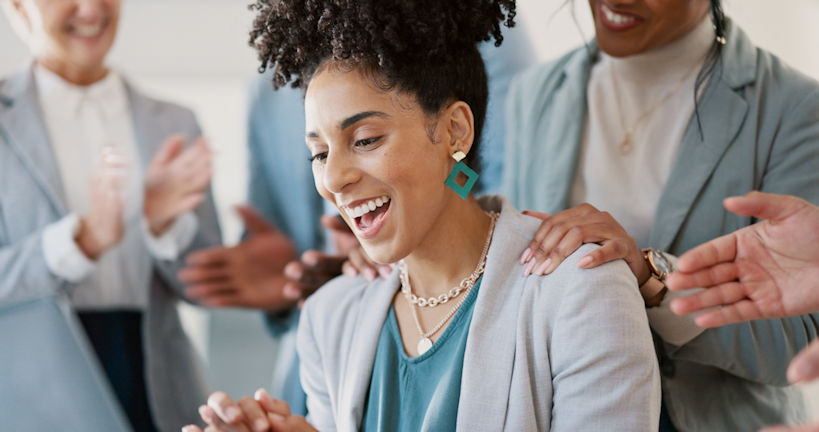 A woman smiling being congratulated by her coworkers around her.