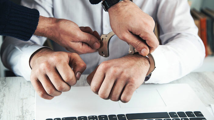 Someone being handcuffed while on the computer.